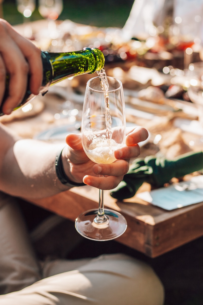 Boisson pétillante servie dans une flûte, table dressée en arrière-plan pour repas extérieur.